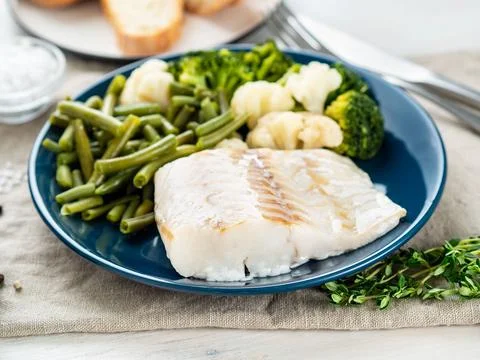 Boiled sea fish cod fillet with vegetables on blue plate, grey wooden table.. Stock Photos