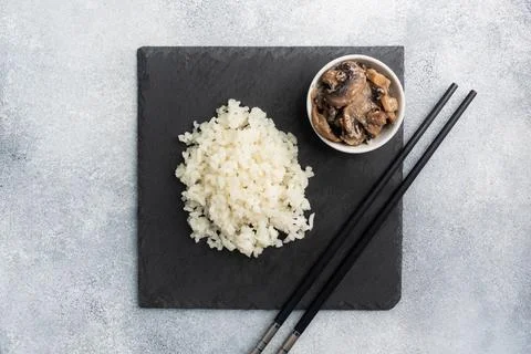 Boiled white rice and mushrooms in sour cream on a black stand with chopsti.. Foto stock