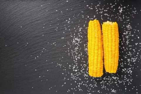 Boiled yellow two corn cob and sifting sea salt served over black slate stone 스톡 사진