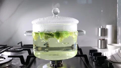 Boiling broccoli in a transparent glass pot on a stove during slow cooking Stock Footage 345426423