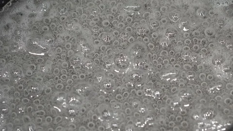 Boiling a clear liquid in a black saucepan, close-up Stock Footage 126316602