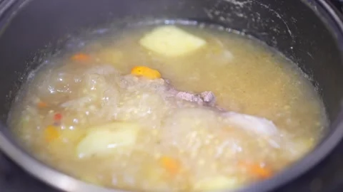 Boiling homemade soup with vegetables bubbles inside a black pot. 動画素材 345740943