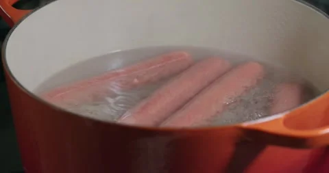 Boiling hot dogs in a orange pot in slow motion Stock Footage 313457629