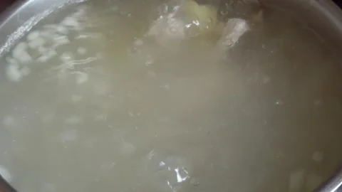 Boiling meat broth with vegetables in a pot top view close up Видео 333622399