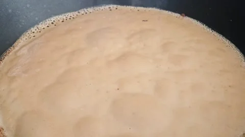 Boiling milk in a black frying pan creates frothy bubbles Stock Footage 333779130
