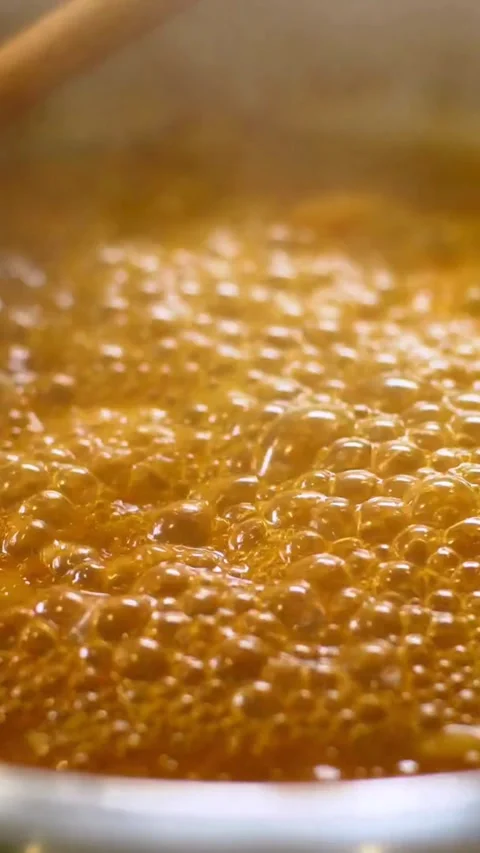 Boiling orange liquid bubbles in pot with wooden spoon Stock Footage 334184985