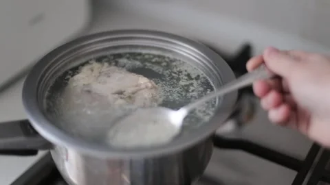 A boiling pot of chicken broth and chicken foam. A woman uses a spoon to collect Stock-Footage 262422010
