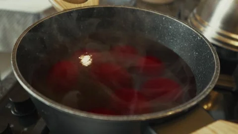 Boiling red eggs in a black pot on a stove, steam rising from the surface, Vídeo Stock 332736919
