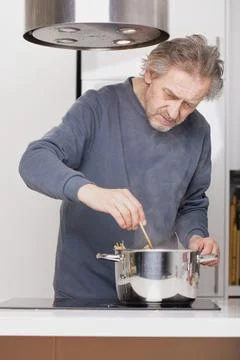 Boiling spaghetti in pot on kitchen hob for lunch or dinner of older man Stock Photos