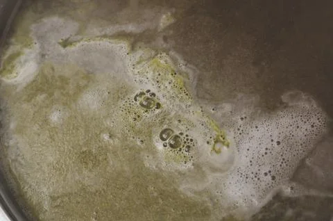 The boiling surface of the beer after laying the green pressed hop. Craft bee Stock Photos
