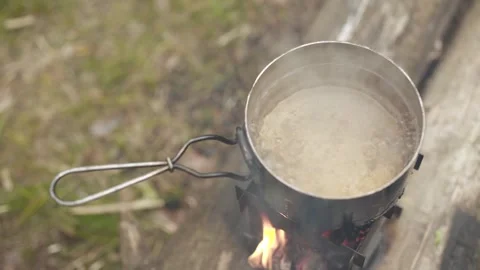 Boiling water in camping pot standing on portable folding wood stove in forest. Video stock 280226783