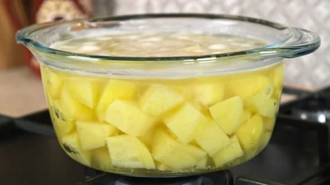 Boiling water with raw potatoes in a glass saucepan over low heat. Stock Footage 191024558