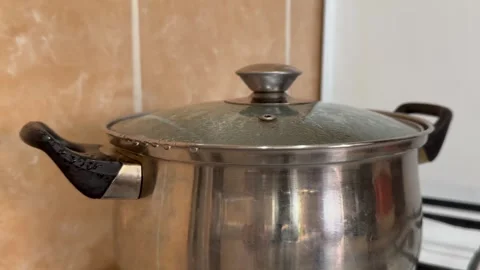 Boiling water splashes out of a metal saucepan from under the lid in the kitchen Stock Footage 255037217
