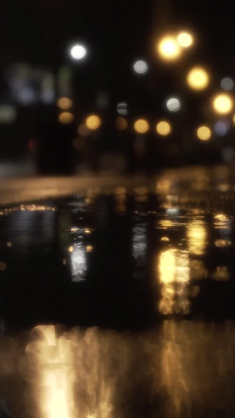 Bokeh city lights reflecting in a rain puddle on a dark, wet street at night Stock Footage 344242271