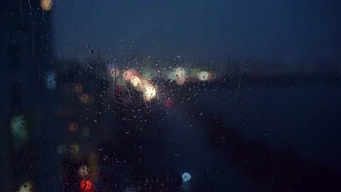Bokeh of city lights through raindrops flowing down the glass. Video stock 199104239