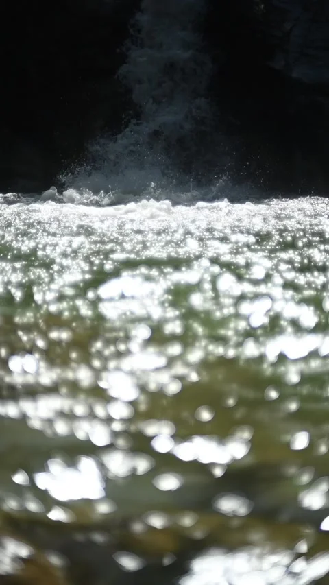 Bokeh of sunlight reflections on a pond in front of a waterfall, slow motion Stock Footage 260870324