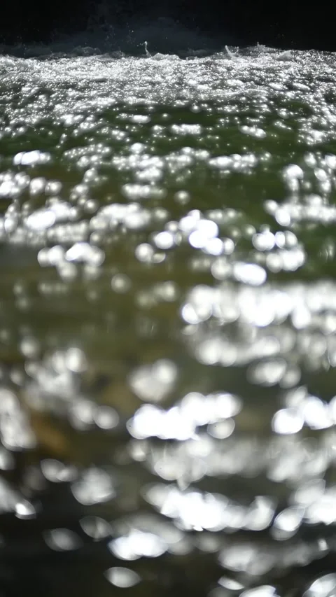 Bokeh of sunlight reflections on a pond in front of a waterfall, slow motion Video stock 260870331