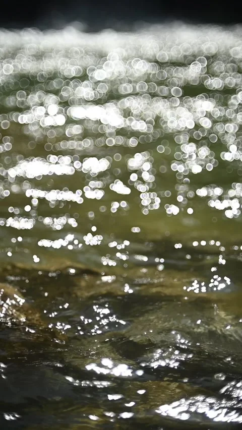 Bokeh of sunlight reflections on a pond in front of a waterfall, slow motion Stock Footage 260870352
