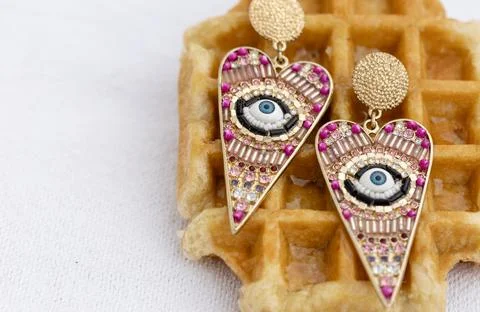 Bold gold earrings with eye patterns on waffle background, copy space. Stock Photos