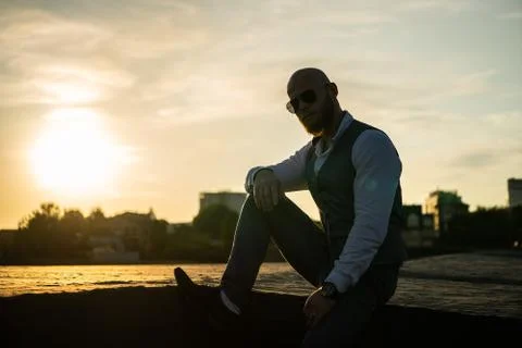 Bold Guy with a stylish beard and sunglasses on a blurred city background during Stock Photos