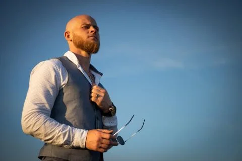 Bold Guy with a stylish beard and sunglasses on a sky background during sunset Stock Photos