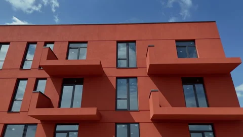 Bold red apartment facade features projecting balconies and dark windows, Modern Vidéo 344646994