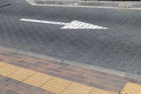 A bold white arrow points right along a paved walkway in a bustling urban a.. Фото