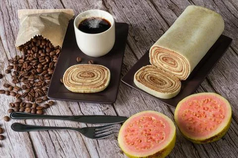 Bolo de rolo slice surrounded by cutlery, guava, cup and coffee beans. Stock Photos