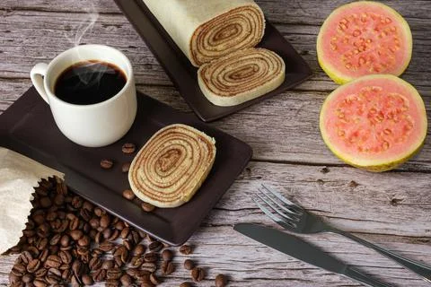 Bolo de rolo slice surrounded by guava, cutlery, cup and coffee beans. Stock Photos