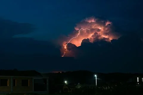Bolt of lightning strikes the ground from the top of a towering thundercloud Stock Photos