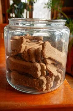 Bone-shaped dog biscuits in an open glass jar on a wooden table Stock Photos