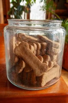 Bone-shaped dog biscuits in an open glass jar on a wooden table Stock Photos