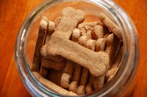 Bone-shaped dog biscuits in an open glass jar on a wooden table Stock Photos