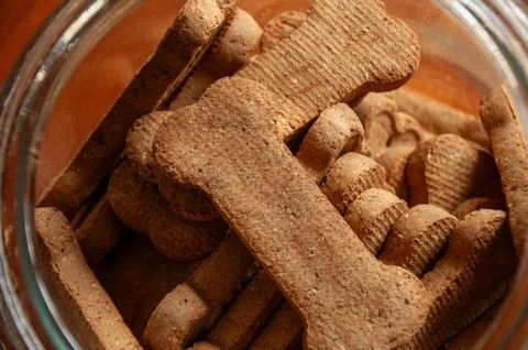 Bone-shaped dog biscuits in an open glass jar on a wooden table Stock Photos