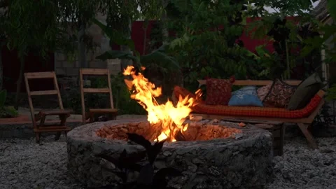 Bonfire burns in a stone pit with wooden chairs and cushioned sofa Stock Footage 344583151