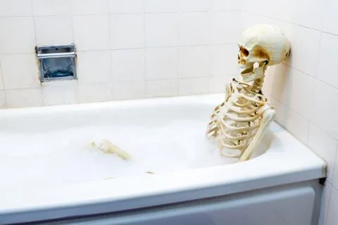 Bony skeleton taking a bubble bath in a grungy off-white dirty tub Foto stock
