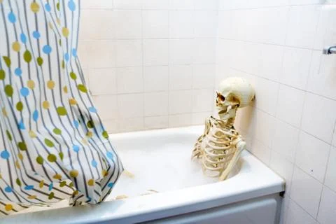 Bony skeleton taking a bubble bath in a grungy off-white dirty tub Stock Photos