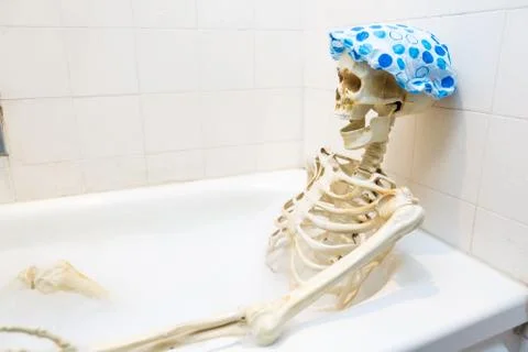 Bony skeleton taking a bubble bath in a grungy off-white dirty tub Stock Photos