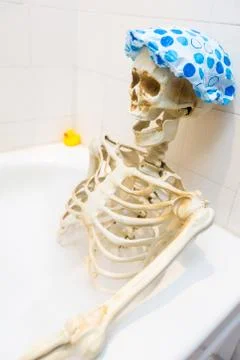 Bony skeleton taking a bubble bath in a grungy off-white dirty tub Stock Photos