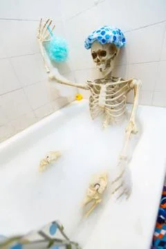 Bony skeleton taking a bubble bath in a grungy off-white dirty tub Stock Photos