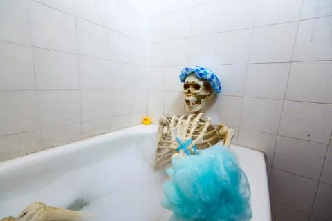 Bony skeleton taking a bubble bath in a grungy off-white dirty tub Stock Photos