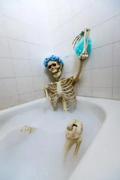 Bony skeleton taking a bubble bath in a grungy off-white dirty tub Stock Photos
