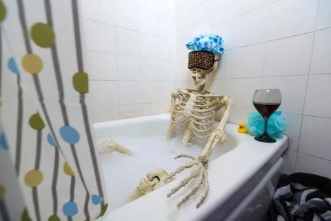 Bony skeleton taking a bubble bath in a grungy off-white dirty tub Foto stock