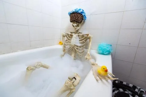 Bony skeleton taking a bubble bath in a grungy off-white dirty tub Stock Photos