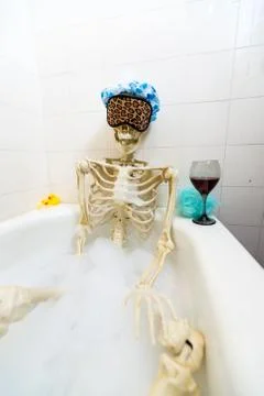 Bony skeleton taking a bubble bath in a grungy off-white dirty tub Stock Photos
