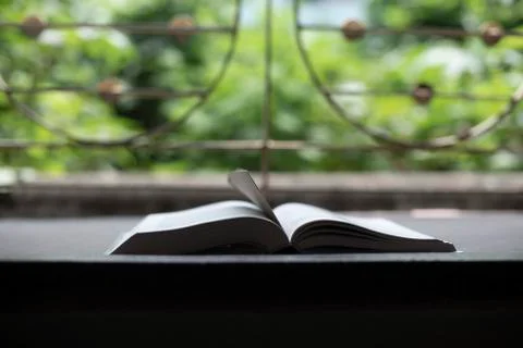 A book is kept open in front of a window with a page mark in a green backgrou Stock Photos