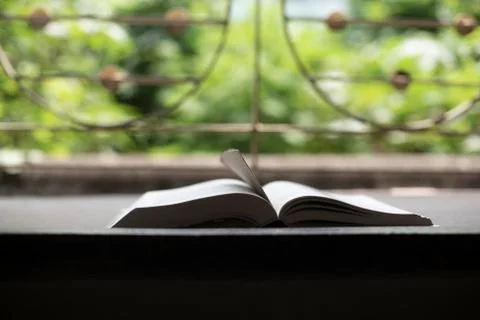 A book is kept open in front of a window with a page mark in a green backgrou Stock Photos