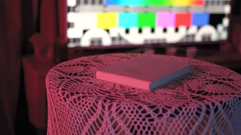 Book is lying on the table in a colored light.behind her is TV that doesn't work Stock Footage 128457728
