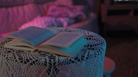 Book is lying on the table in a colored light.behind her is TV that doesn't work Stock Footage 128458240