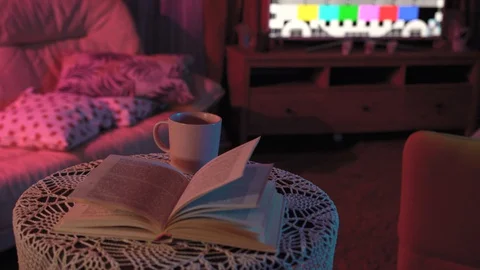 Book is lying on the table in colored light.behind her is a TV that doesn't work Stockbeeldmateriaal 128460641